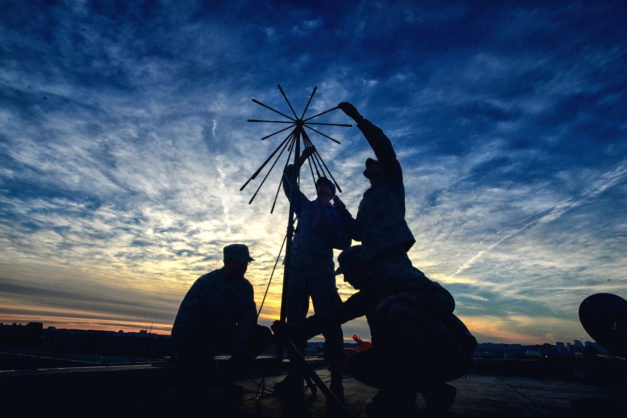 Communications team raising a tactical antenna on a rooftop at sunset